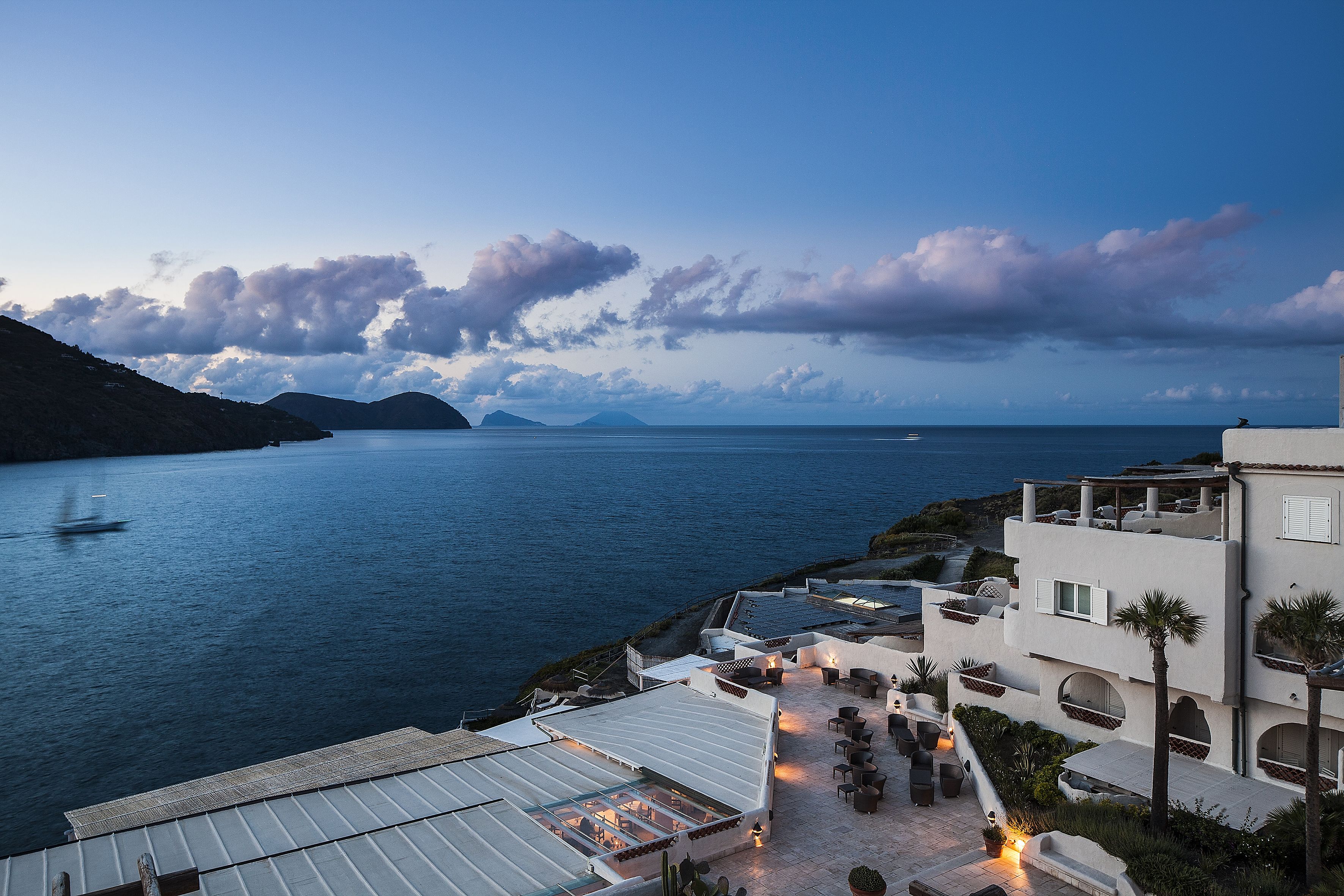 A coastal hotel with a terrace overlooking the sea, featuring outdoor seating and a view of the ocean.