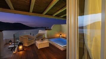 Un terrazzo in legno con mobili in vimini e una vasca idromassaggio, con vista su un lago e montagne al crepuscolo.