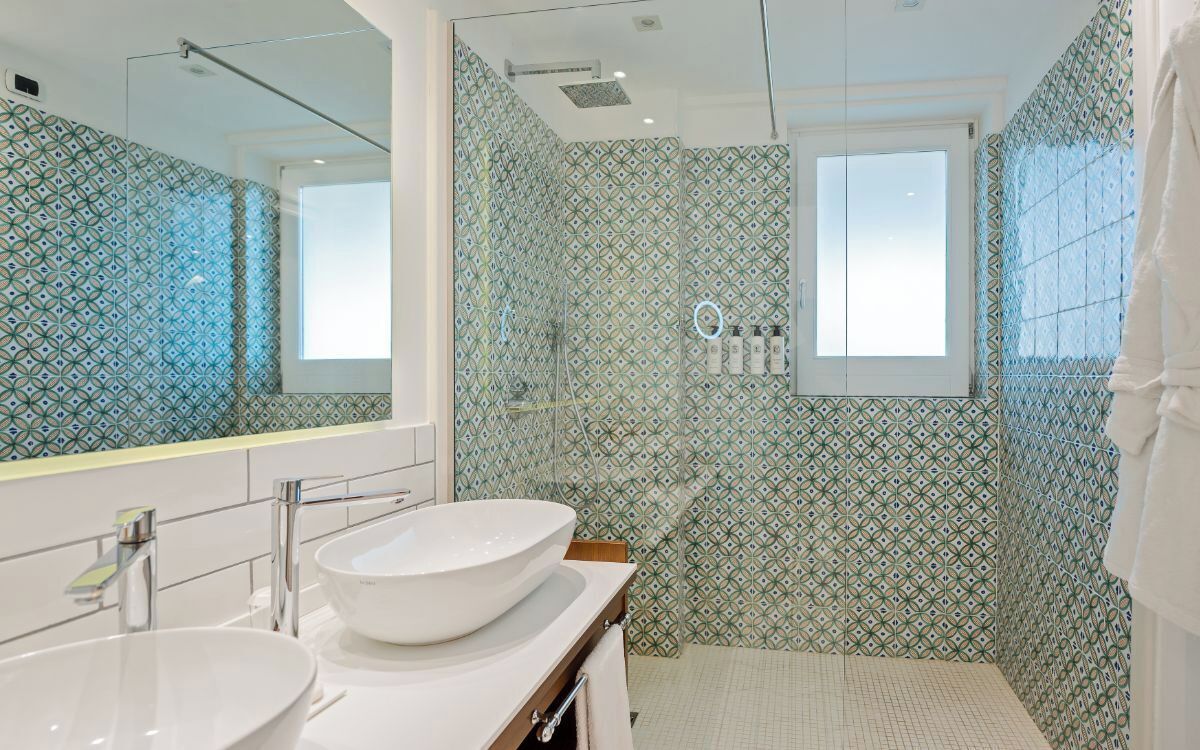 Een moderne badkamer met een grote spiegel, twee wasbakken, een douche en betegelde wanden.
