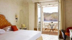 Une chambre d’hôtel avec un lit, une petite table et une chaise, et une vue sur la mer par une porte ouverte.