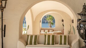 Un coin salon confortable avec vue sur la mer, grâce à une fenêtre en arc de cercle, agrémenté d’une lampe et d’un vase décoratif.