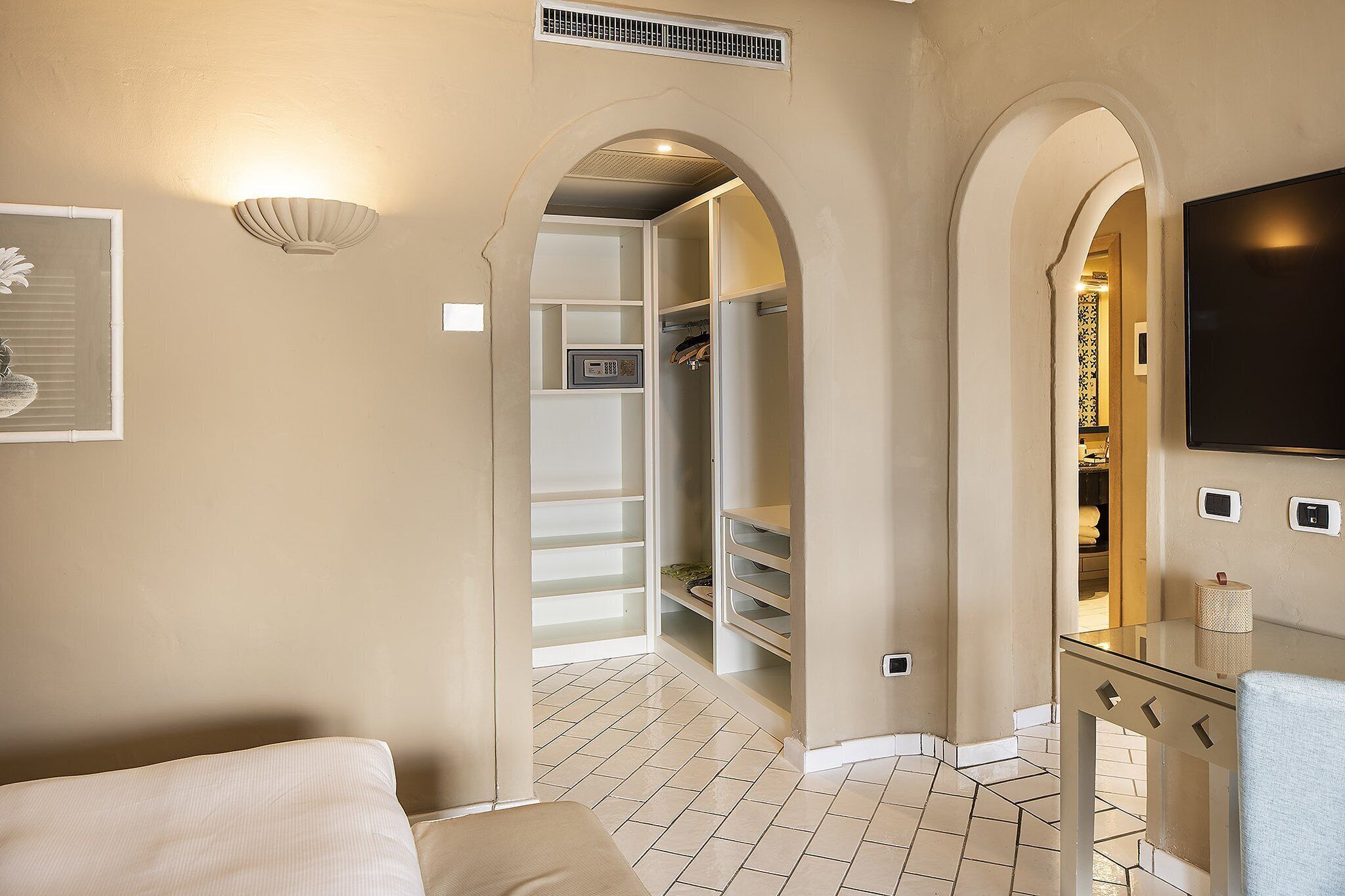Habitación de hotel con cama, mesita de noche, armario y televisor.