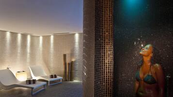 A spa area with two white lounge chairs, a massage table, and a mosaic wall.