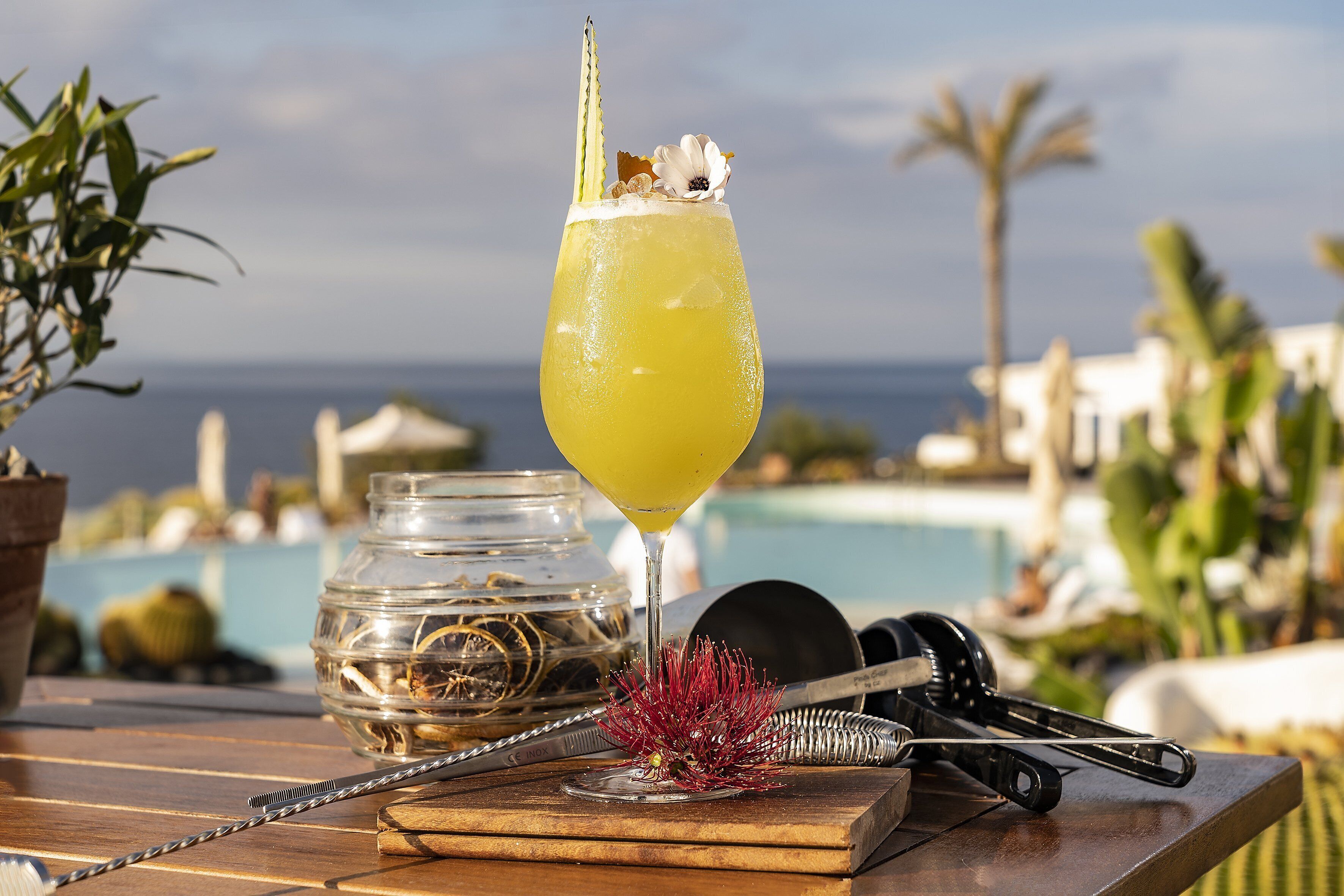 A cocktail glass with a straw and garnish on a wooden table with a pool view in the background.