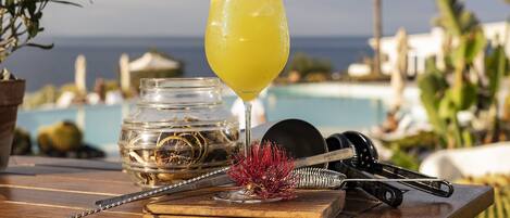 A cocktail glass with a straw and garnish on a wooden table with a pool view in the background.