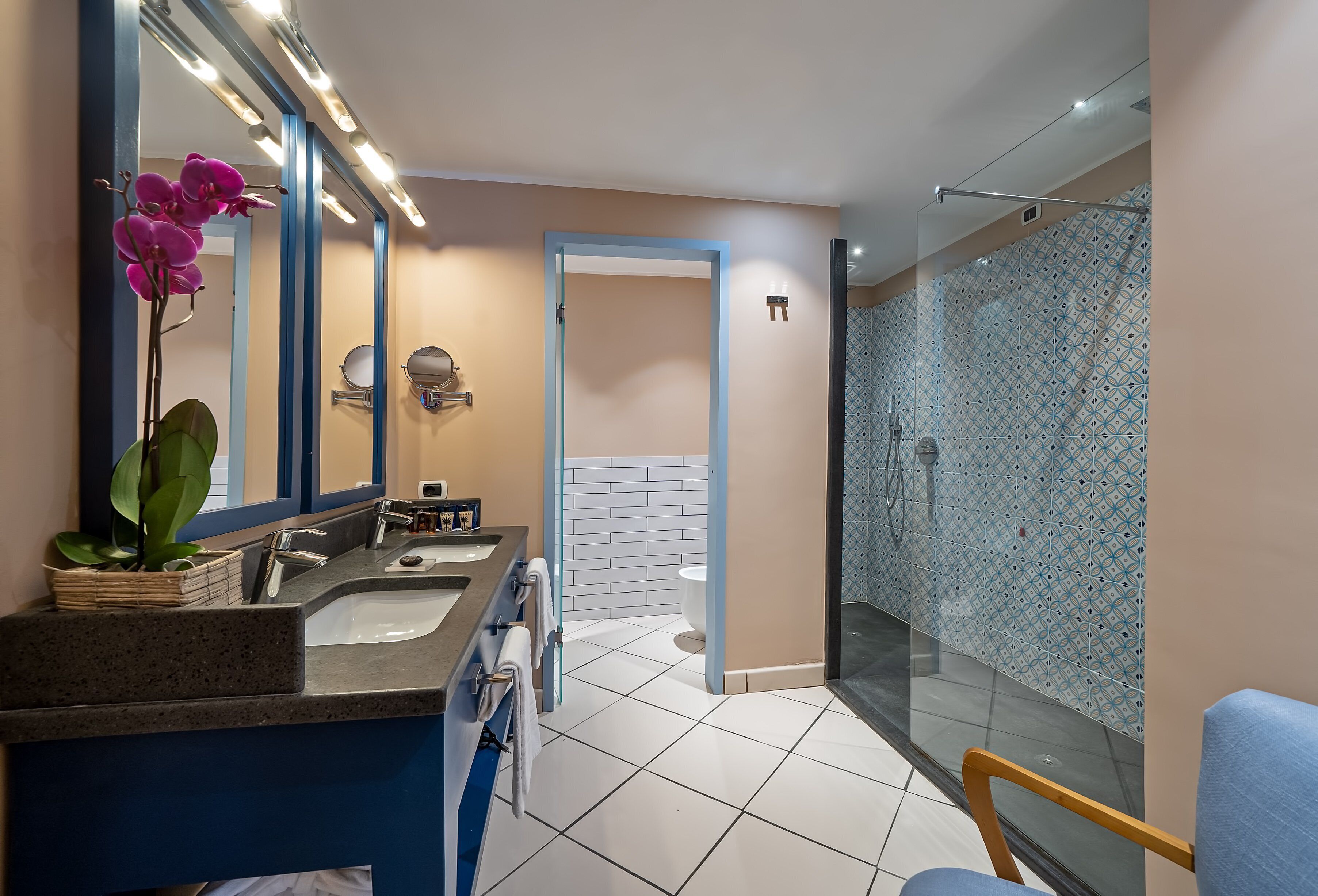 Un bagno moderno con un mobile doppio lavabo, un grande specchio, un'orchidea in vaso e una doccia con piastrelle decorate.