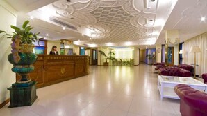 Um hall amplo com balcão de recepção, assentos confortáveis e teto decorativo.