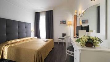 Habitación de hotel con una cama grande, un escritorio con silla, una lámpara de escritorio y un espejo.