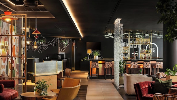 Een moderne barruimte met een bar, zitplaatsen en diverse verlichtingsarmaturen.