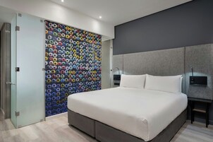 A modern bedroom with a large bed, a gray headboard, and a colorful circular wall decoration.