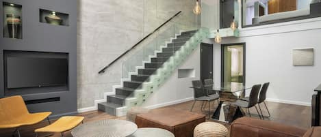 Un salon moderne avec un escalier, des canapés en cuir, une table en verre et des éléments de décoration fixés au mur.