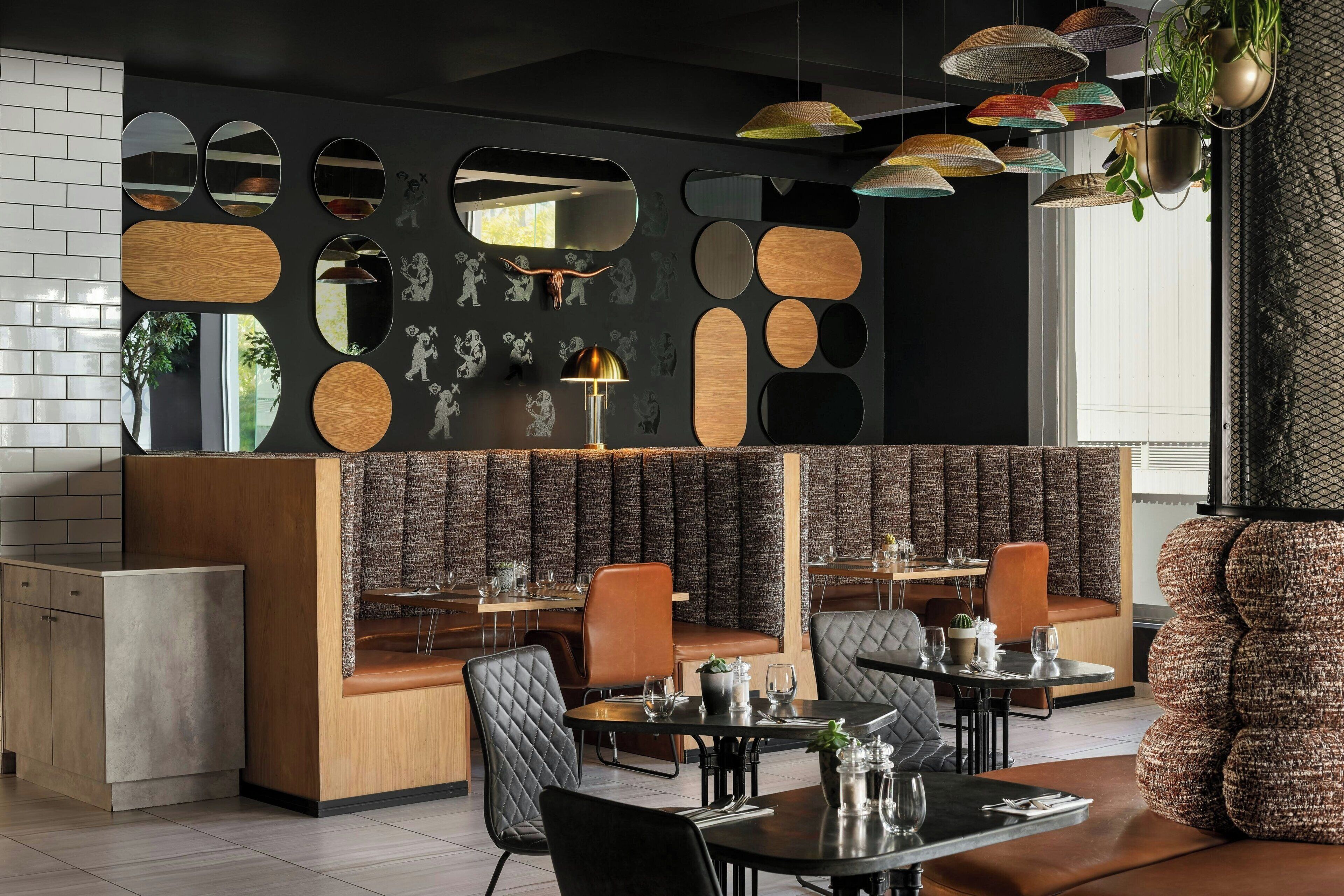 A modern restaurant interior with a black and wood color scheme, multiple seating areas, and decorative mirrors.