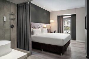 A modern hotel room with a large bed, a separate bathroom, and a view of the city.