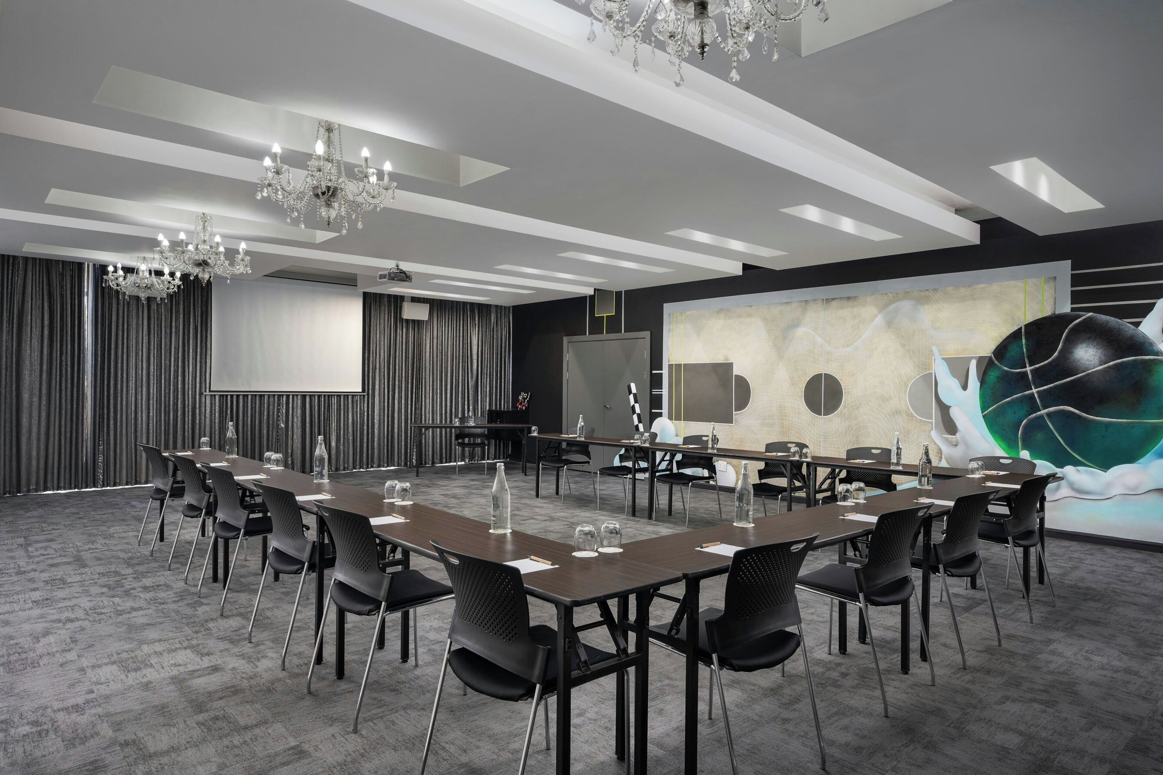 A conference room with a long table, black chairs, a projector screen, and a large abstract painting on the wall.