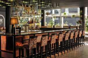 A bar area with a long counter, multiple stools, and a variety of bottles and glasses on shelves.