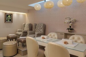 A modern spa room with a glass table, beige upholstered chairs, and a large window.
