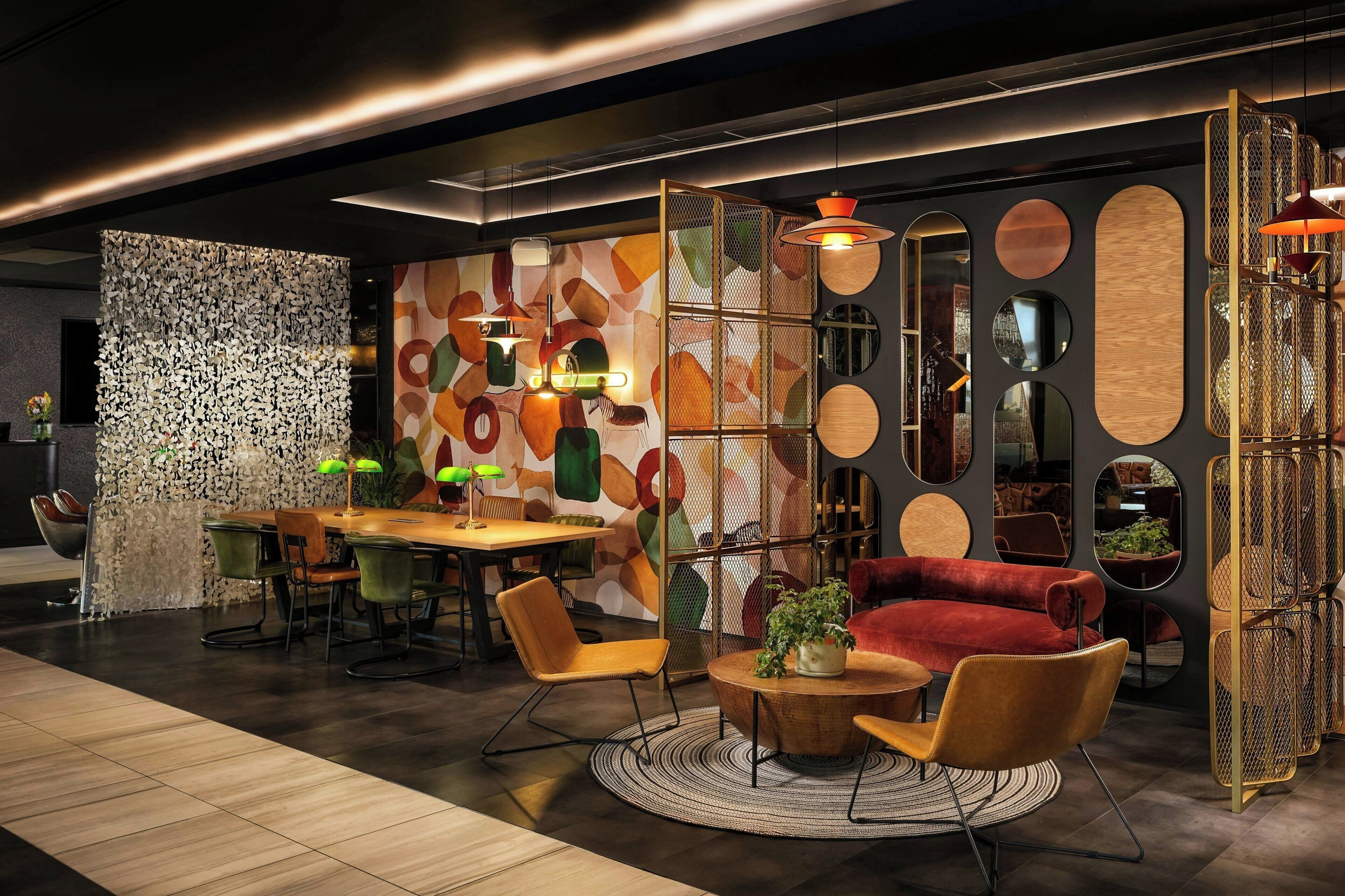Un intérieur moderne avec une table de salle à manger ronde, des chaises, un canapé rouge et un mur décoratif orné de motifs abstraits.
