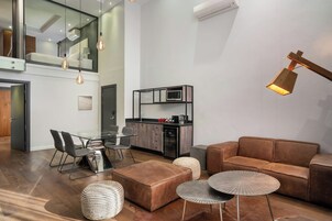 A modern living room with a brown leather sofa, a glass dining table with chairs, and a kitchen area with a microwave.
