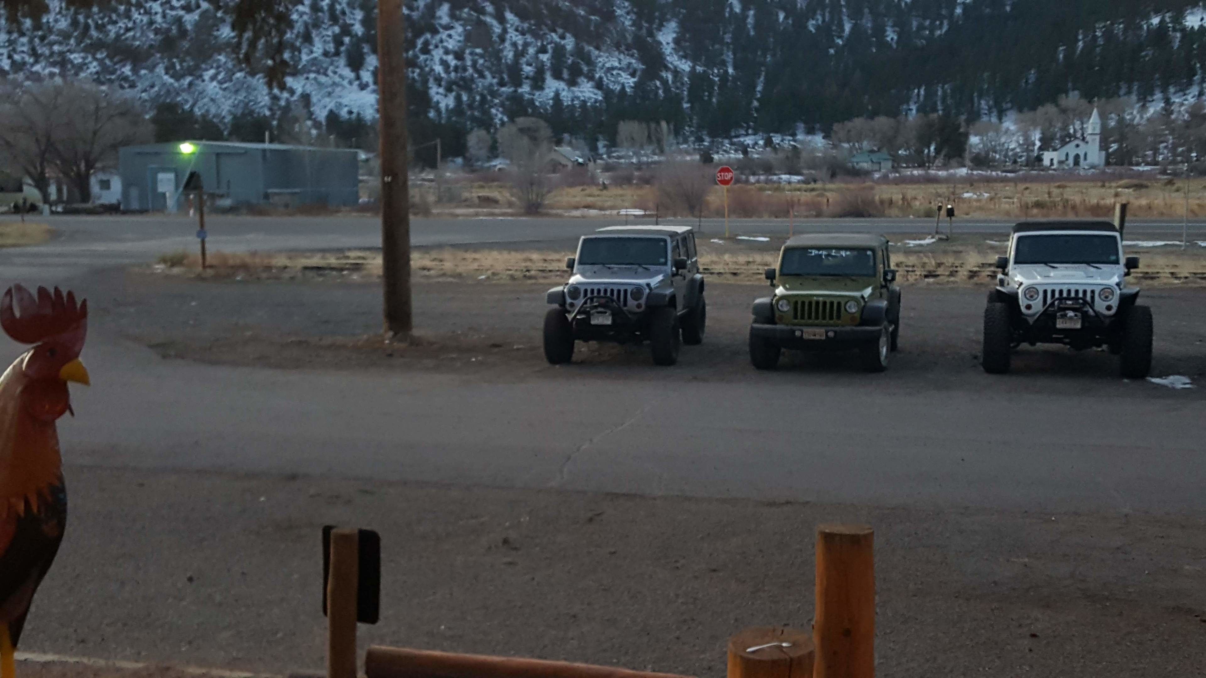 Three off-road vehicles parked on a dirt road with a stop sign in the background.