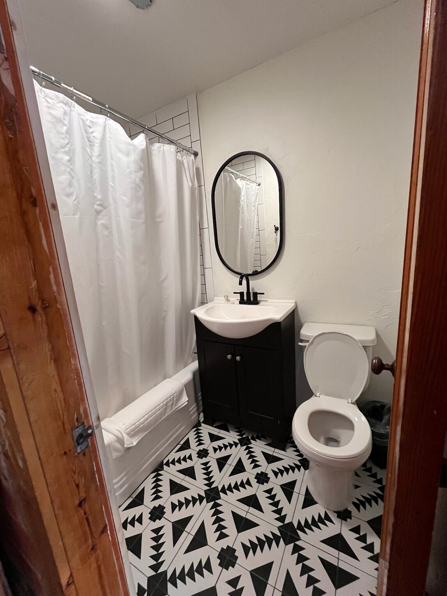 A bathroom with a black and white patterned floor, a white toilet, a black sink with a mirror above it, and a white shower curtain.