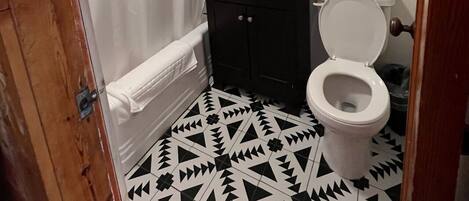 A bathroom with a black and white patterned floor, a white toilet, a black sink with a mirror above it, and a white shower curtain.