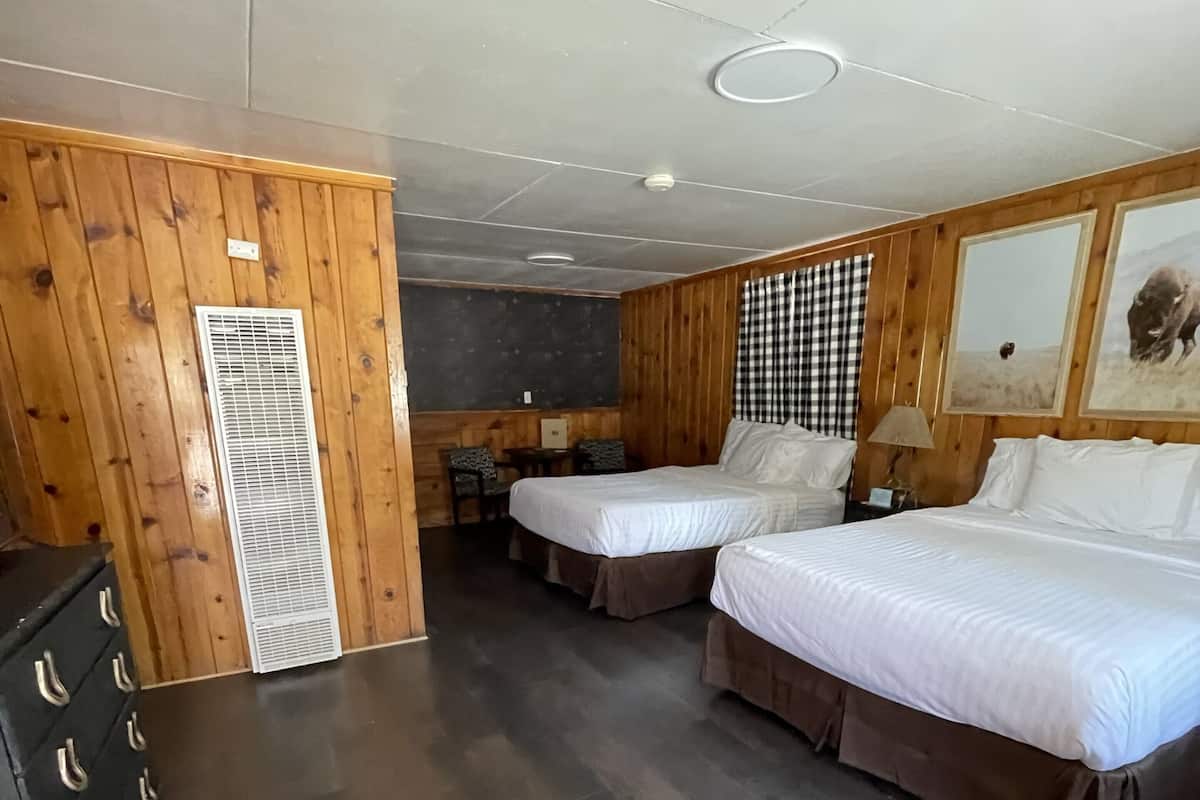 A hotel room with two beds, a desk, a chair, a dresser, and a large window with a view.