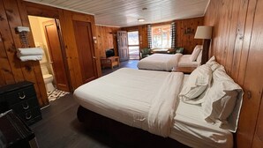 Una habitación con paneles de madera, dos camas, un aparador y una ventana con cortinas.