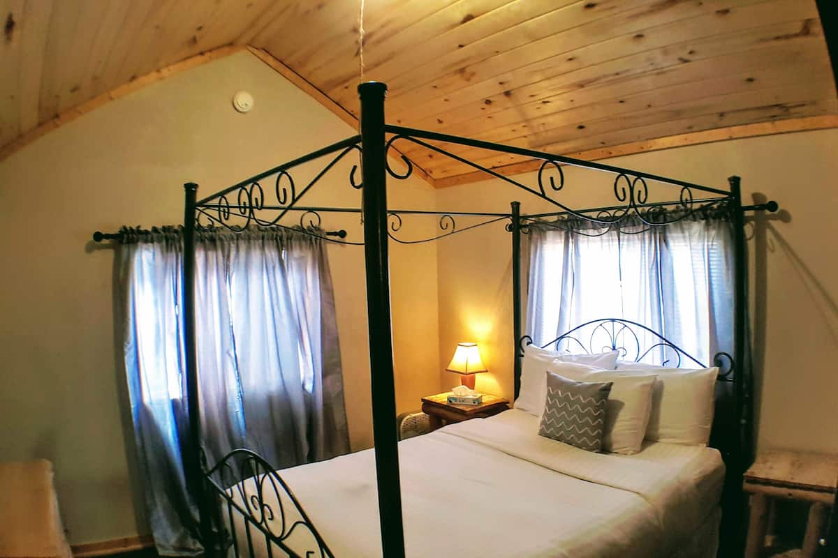 A four-poster bed with curtains, a bedside lamp, and a wooden ceiling.