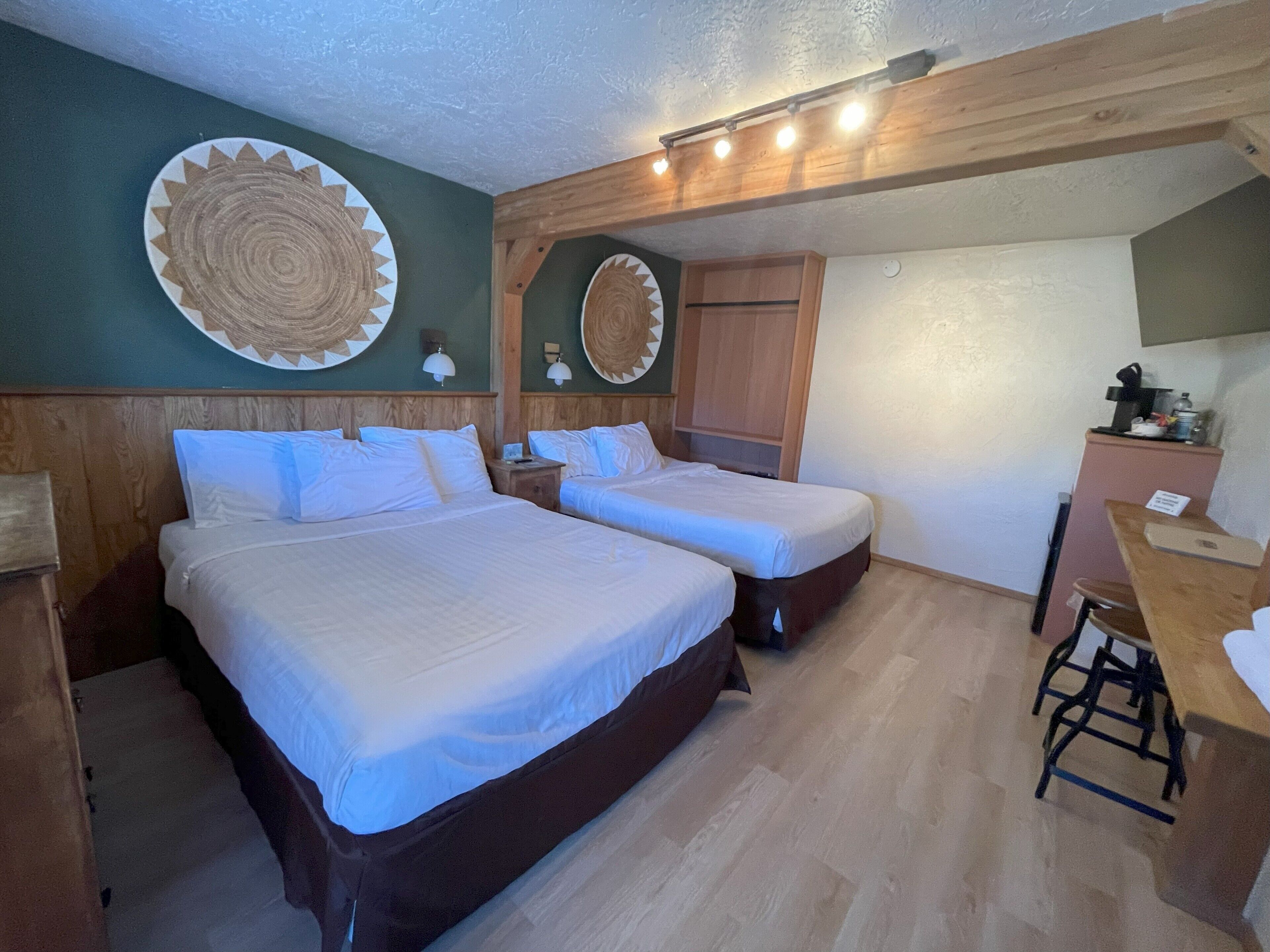 Une chambre avec deux lits, une tête de lit en bois, des éléments de décoration murale, un bureau et une chaise.