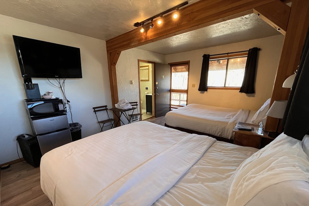 A hotel room with two beds, a flat-screen TV, a microwave, and a small table with chairs.