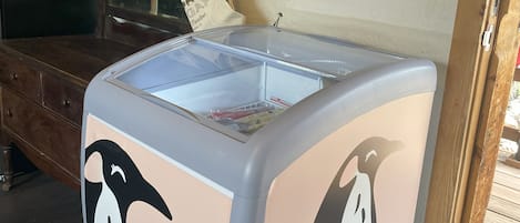 A room with a large ice cream freezer, wooden furniture, and a shelf with hats.