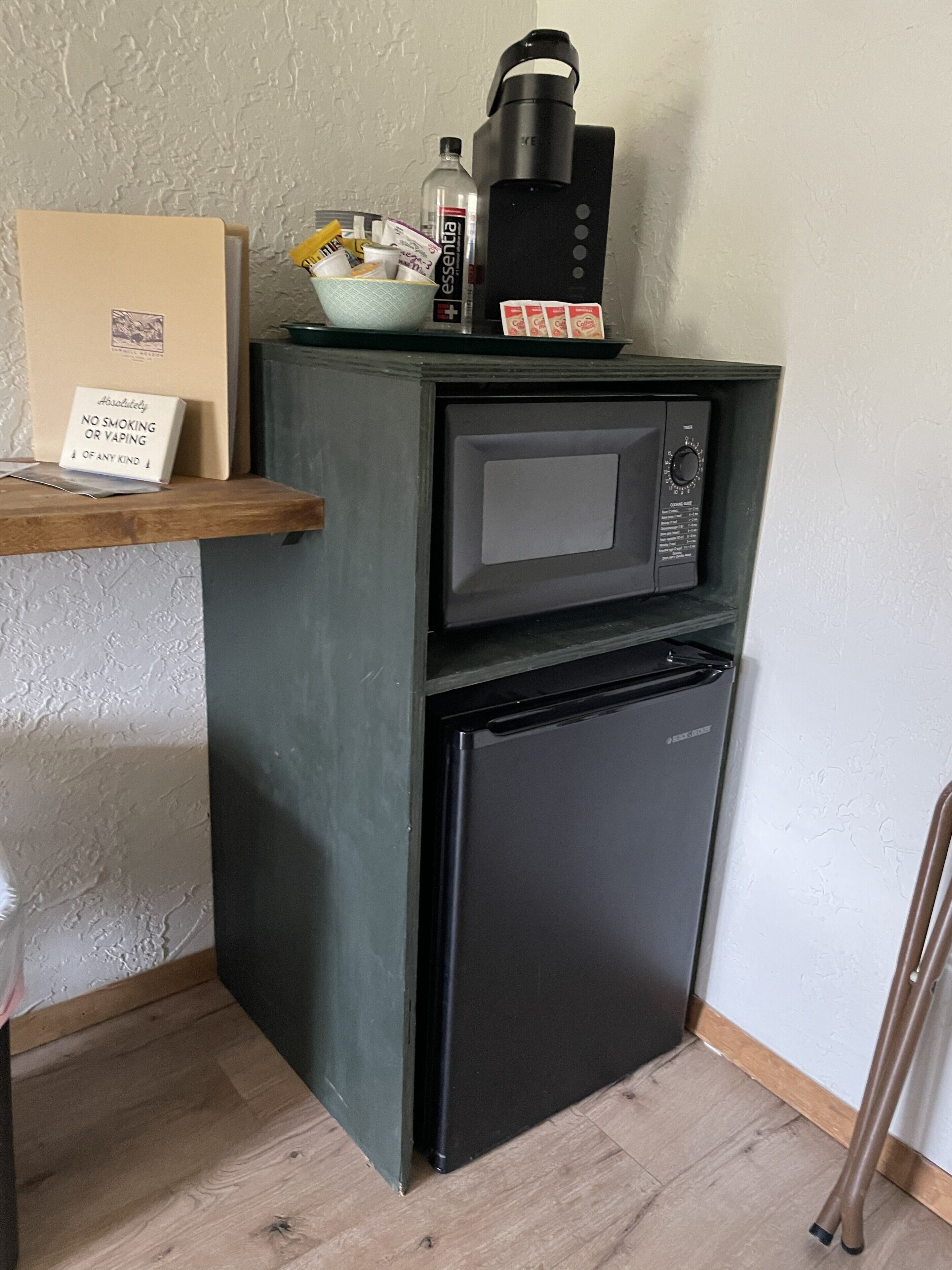 Una kitchenette compacta con microondas, un refrigerador pequeño y una cafetera sobre una estantería.