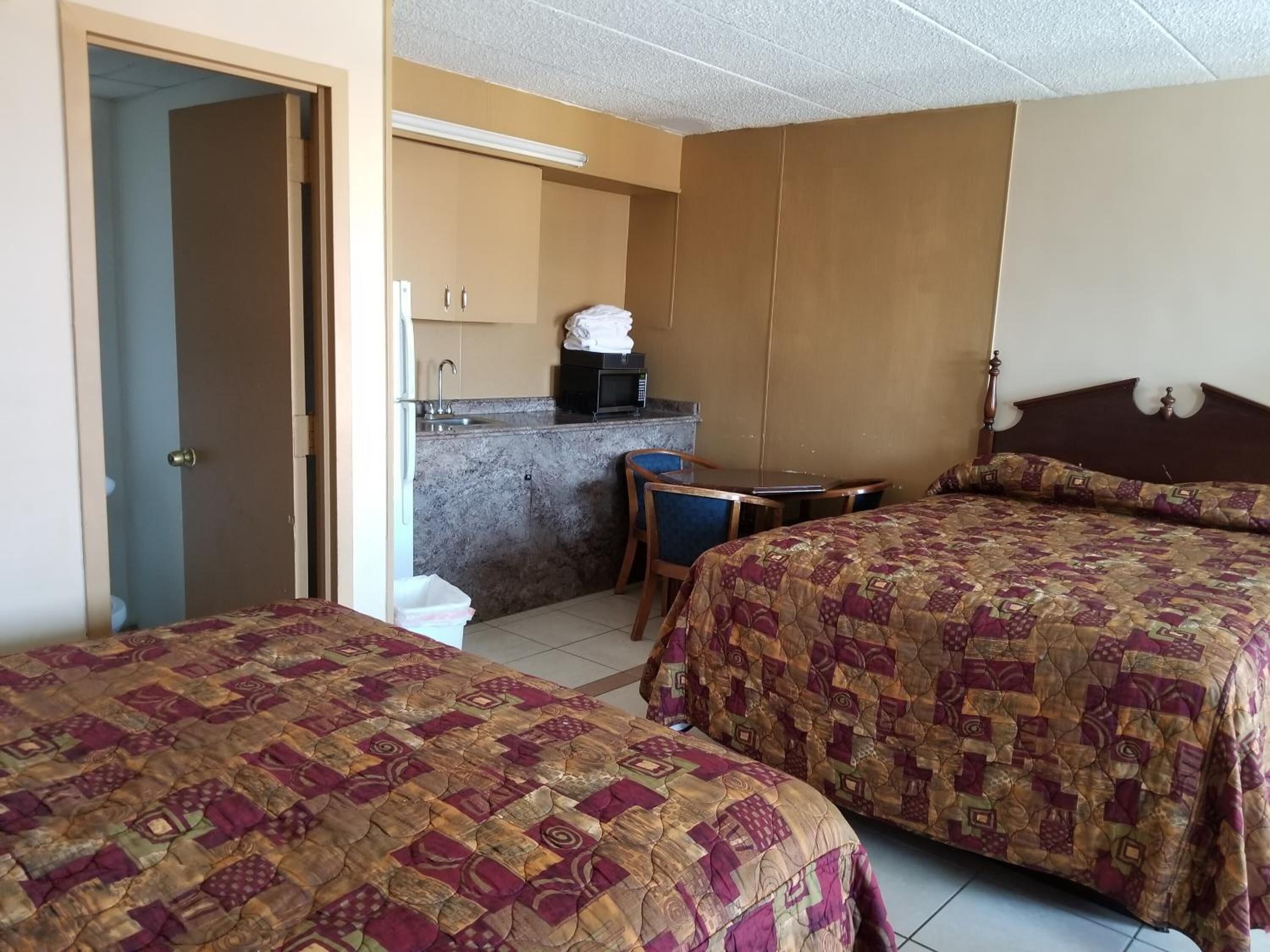A hotel room with two beds, a small kitchenette, and a bathroom.