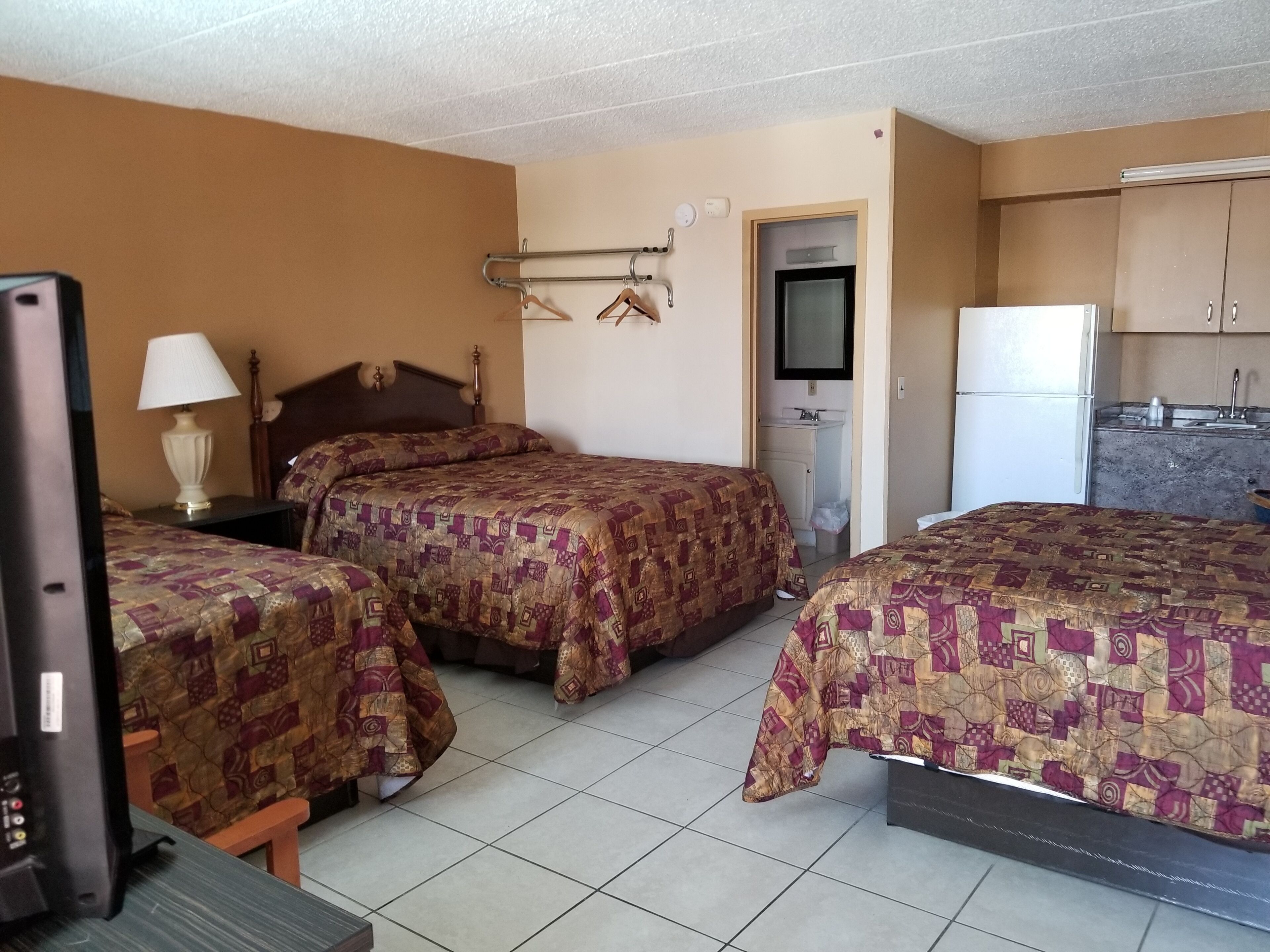 Habitación de hotel con dos camas, televisión, escritorio, lámpara, armario, lavamanos y refrigerador.