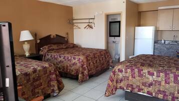 Habitación de hotel con dos camas, televisión, escritorio, lámpara, armario, lavamanos y refrigerador.