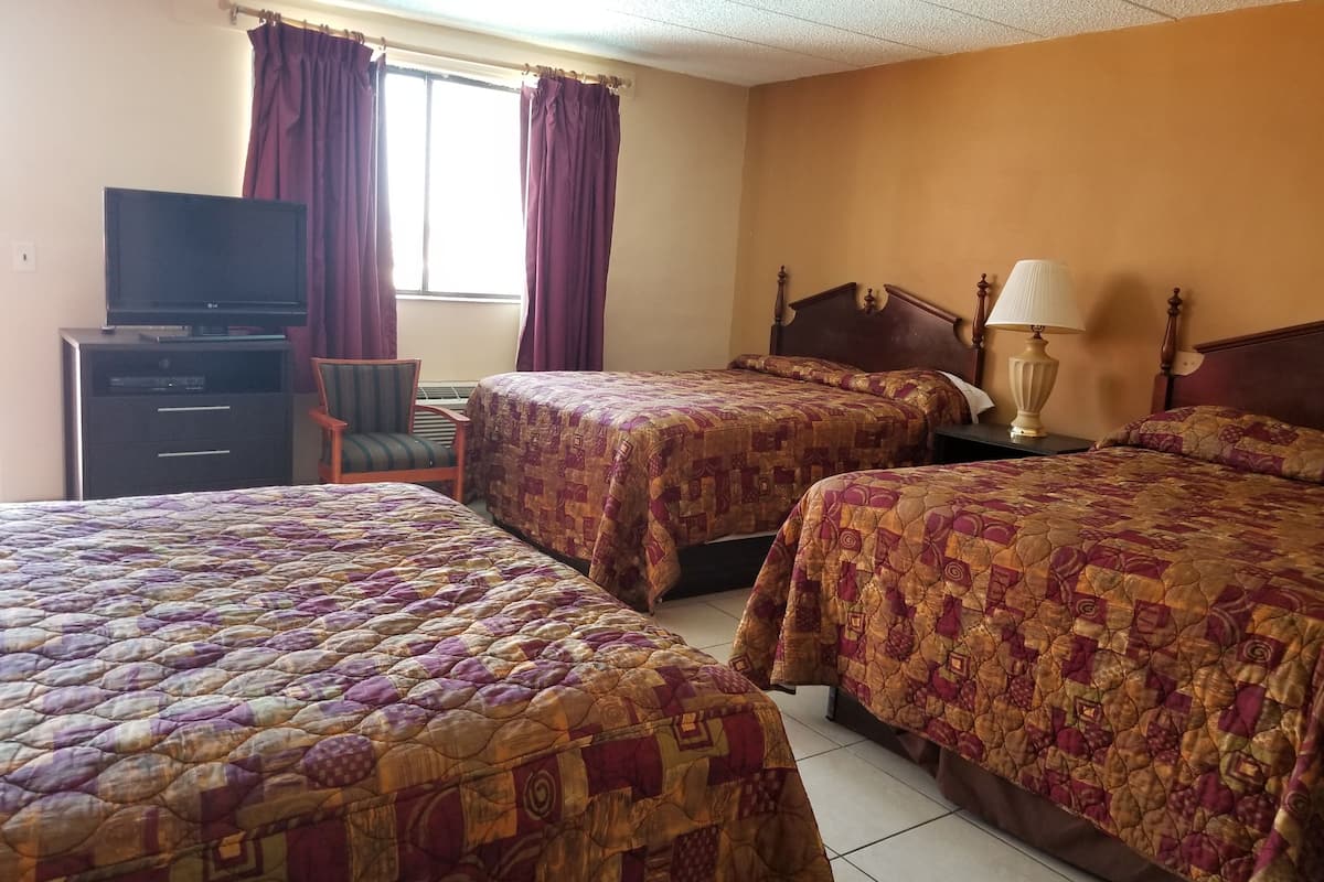 A hotel room with two beds, a TV, a chair, and a window with curtains.