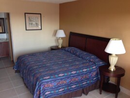 Habitación de hotel con cama, dos mesitas de noche, un cuadro enmarcado en la pared y una puerta que da al baño.