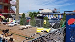 A hotel with a pool area, a fenced parking lot, and a building with a red door in the background.
