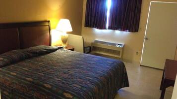 A hotel room with a bed, a nightstand, a lamp, an air conditioning unit, and a door.