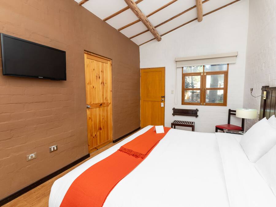 A hotel room with a bed, a television, a wooden door, a window, and a bench.