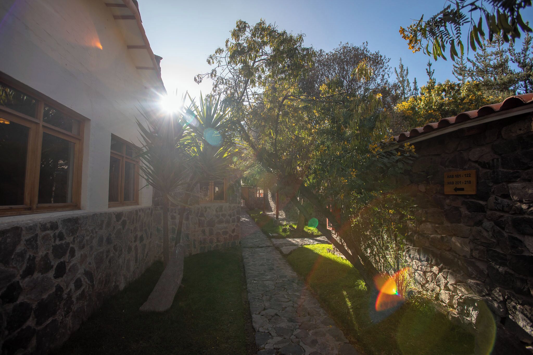 A stone-walled courtyard with a pathway leading to a building with large windows.