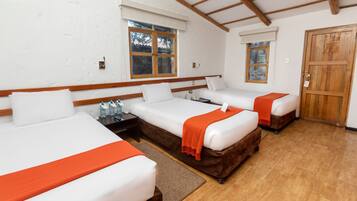 A hotel room with three single beds, wooden beams on the ceiling, white walls, and a wooden door.