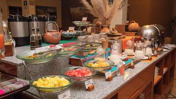 Un buffet proposant une variété de plats et de boissons, notamment des saladiers de fruits et un coin café.