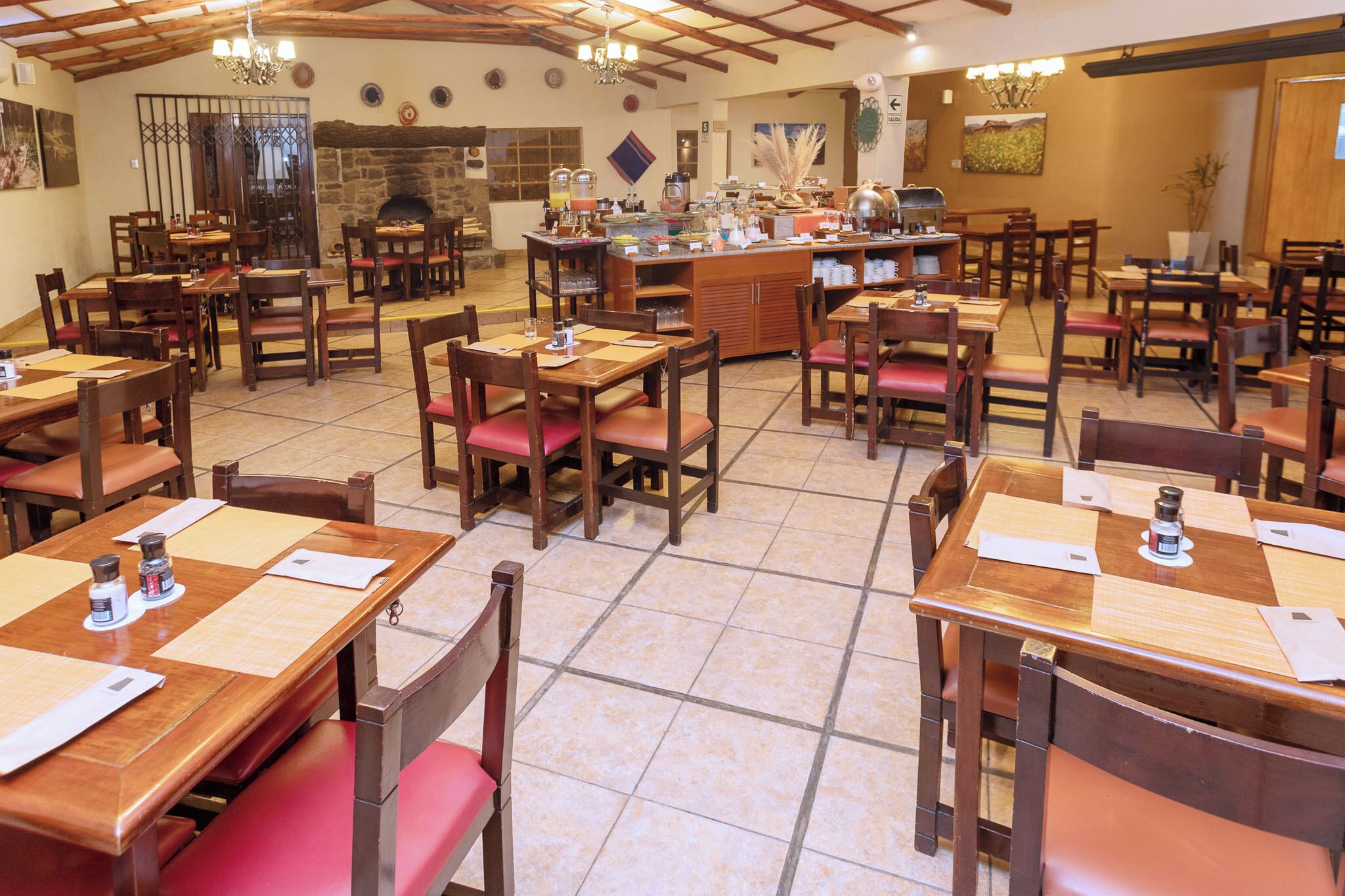 A restaurant with multiple wooden tables and chairs, a central bar area, and a stone fireplace.