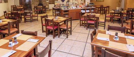 A restaurant with multiple wooden tables and chairs, a central bar area, and a stone fireplace.