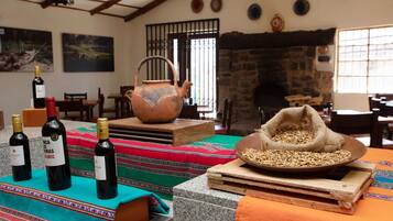 A rustic interior with a stone fireplace, wooden furniture, and a table with wine bottles and a bowl of grains.