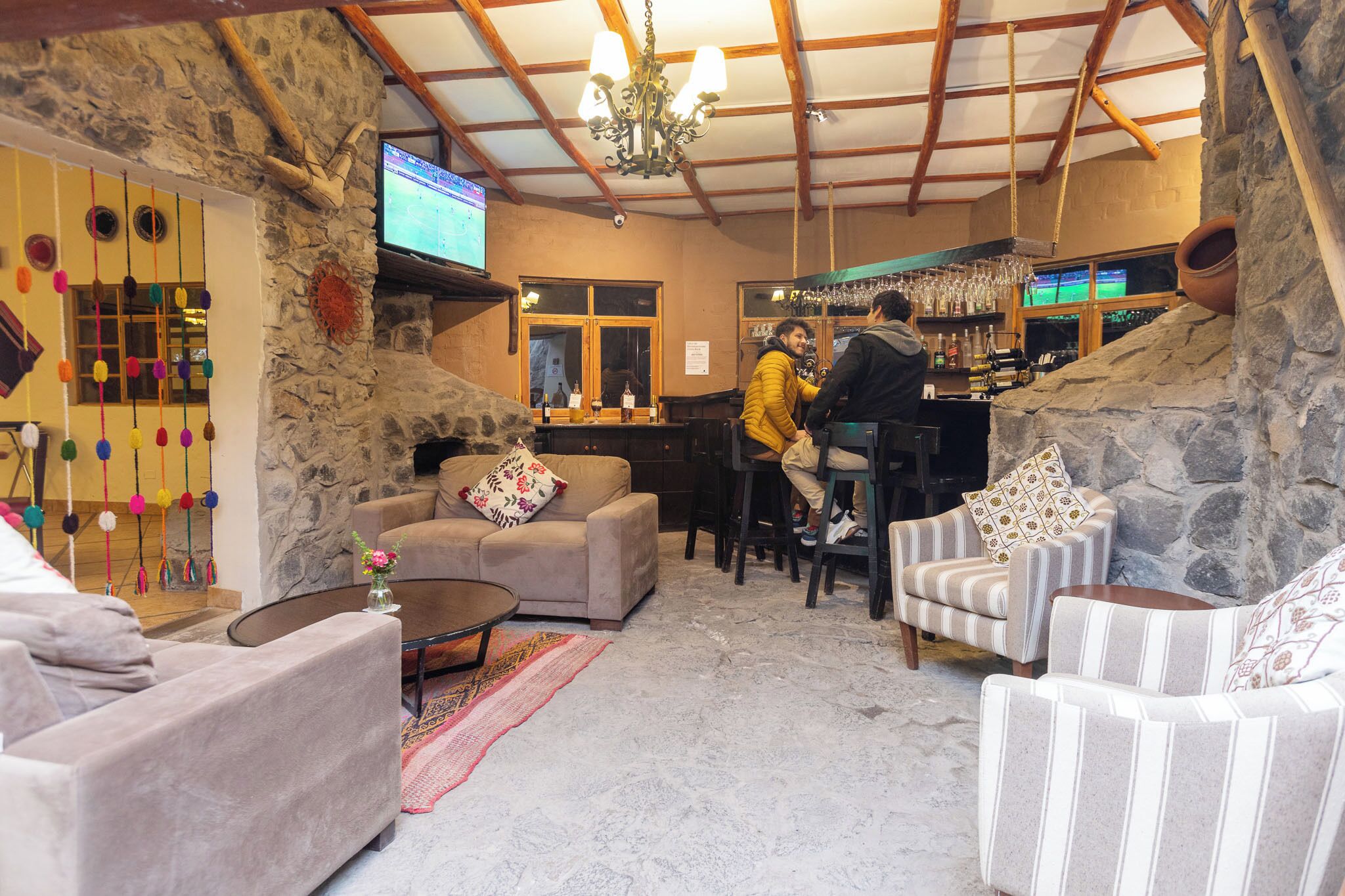 Un rincón acogedor con bar, paredes de piedra, techo de madera y una pantalla de televisión. Ofrece varias opciones de asientos, incluyendo un sofá, sillones y un taburete de bar.