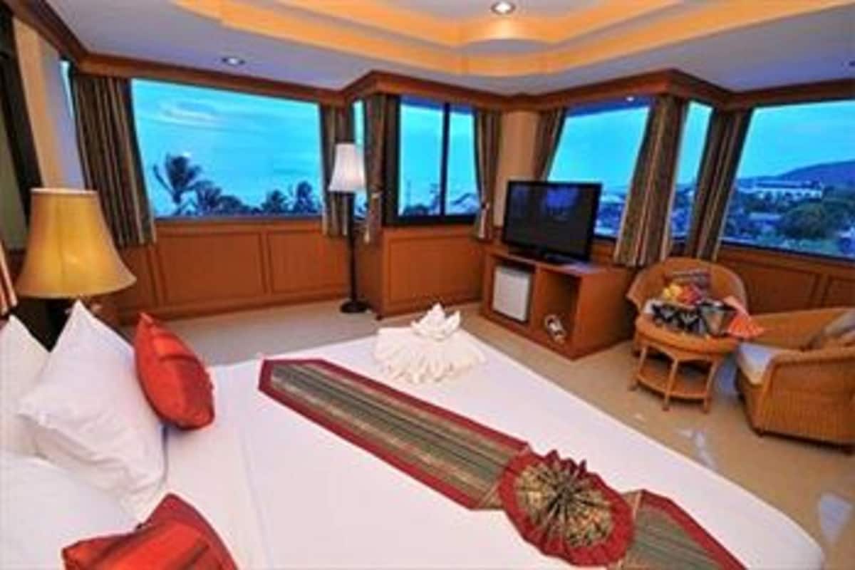 A hotel room with a large bed, a television, a sofa, and a view of the cityscape.
