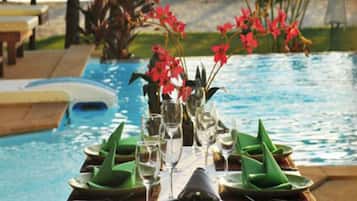 A dining table set for two with a view of a swimming pool.