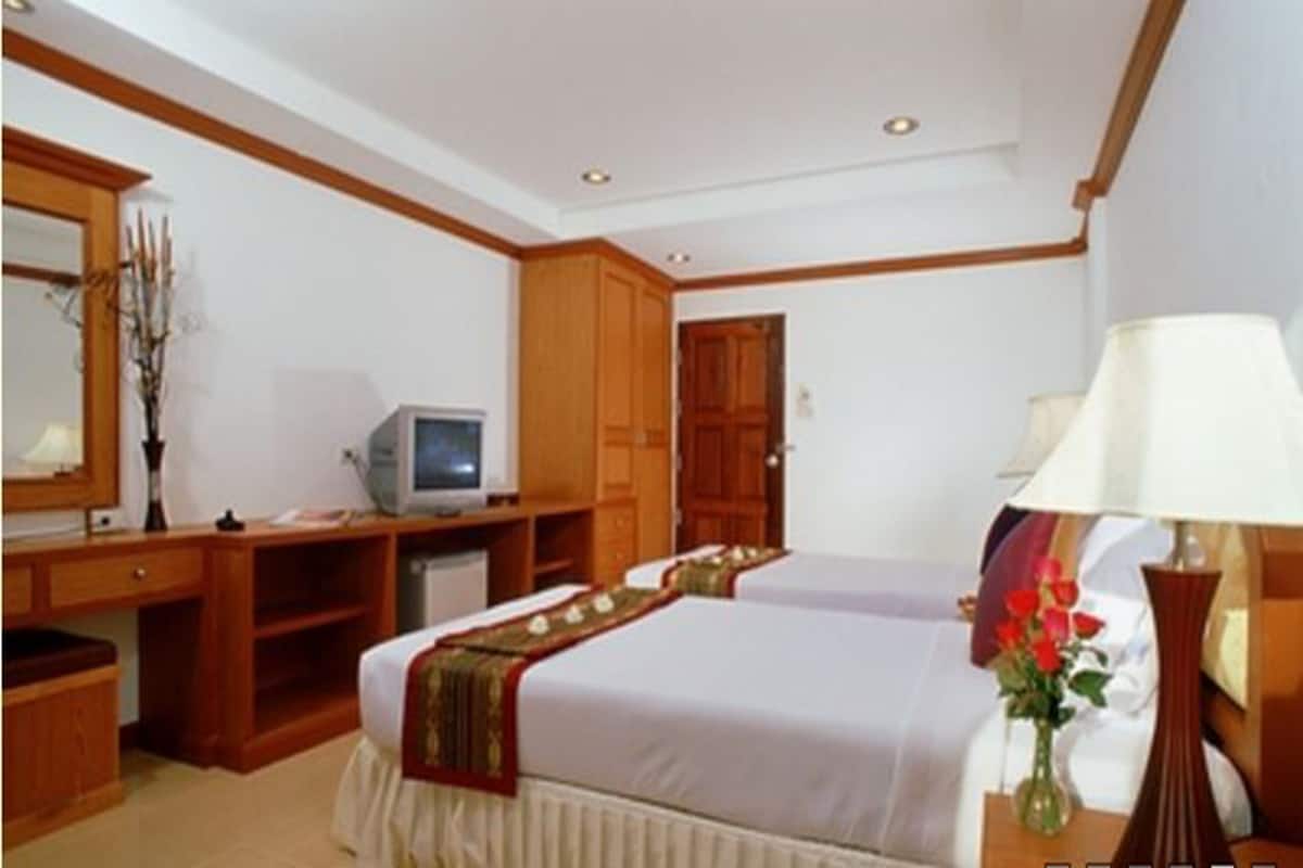 A hotel room with two beds, a desk, a television, and a lamp.